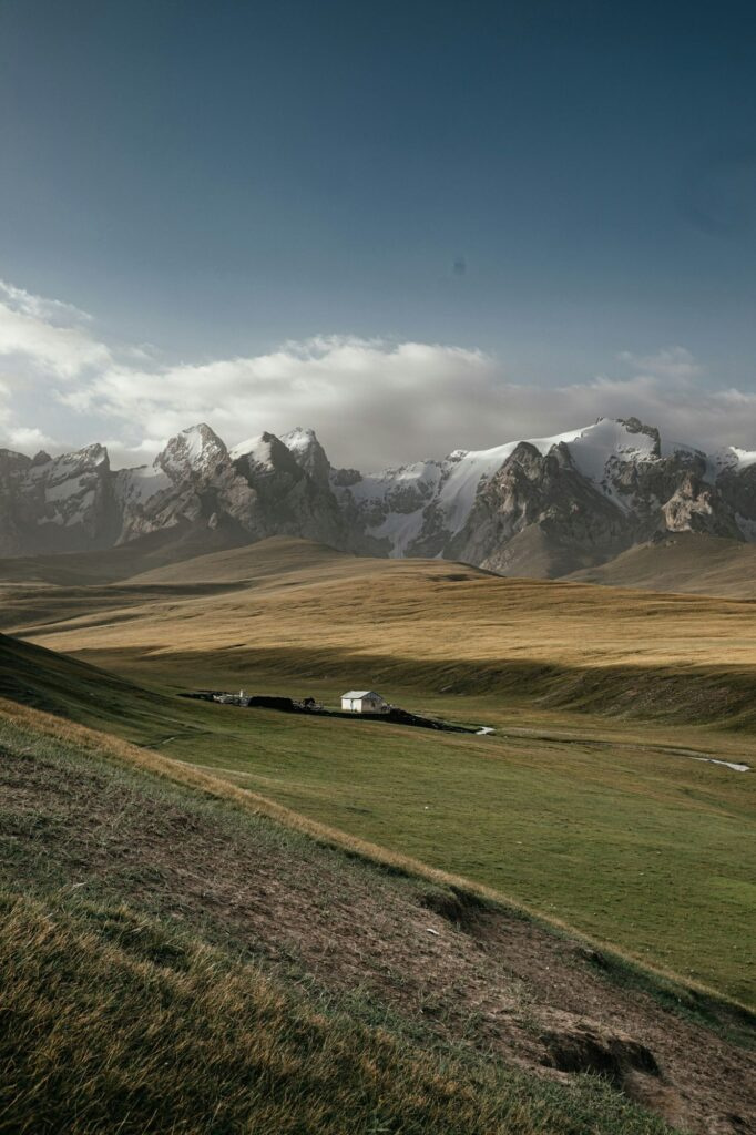 Snow-capped peaks above a green valley with a lone herder house in Kyrgyzstan