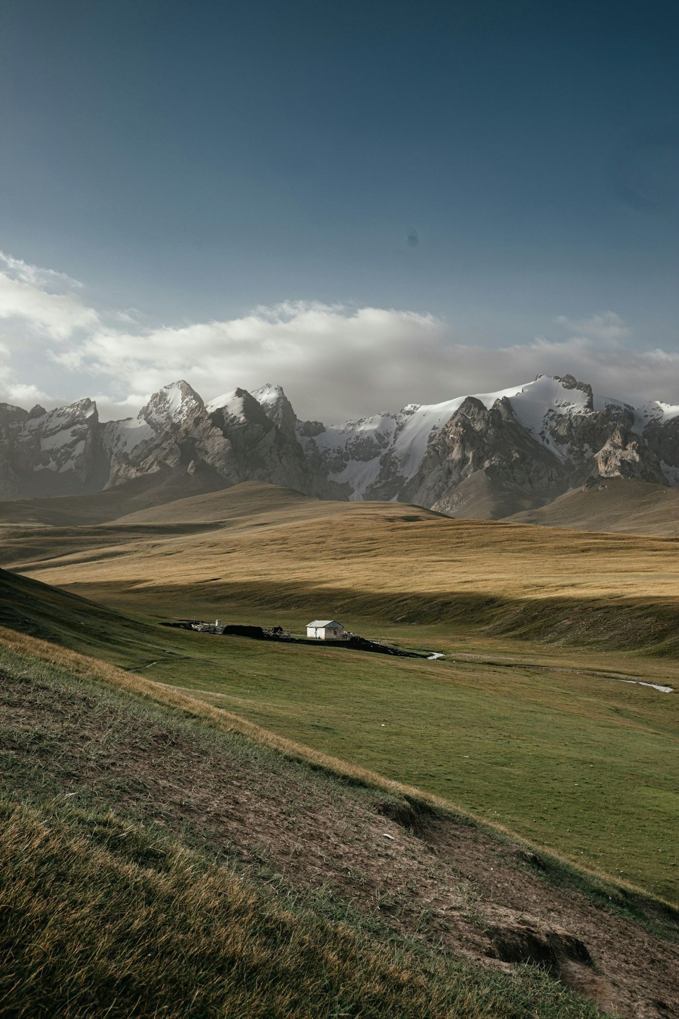 Snow-capped peaks above a green valley with a lone herder house in Kyrgyzstan